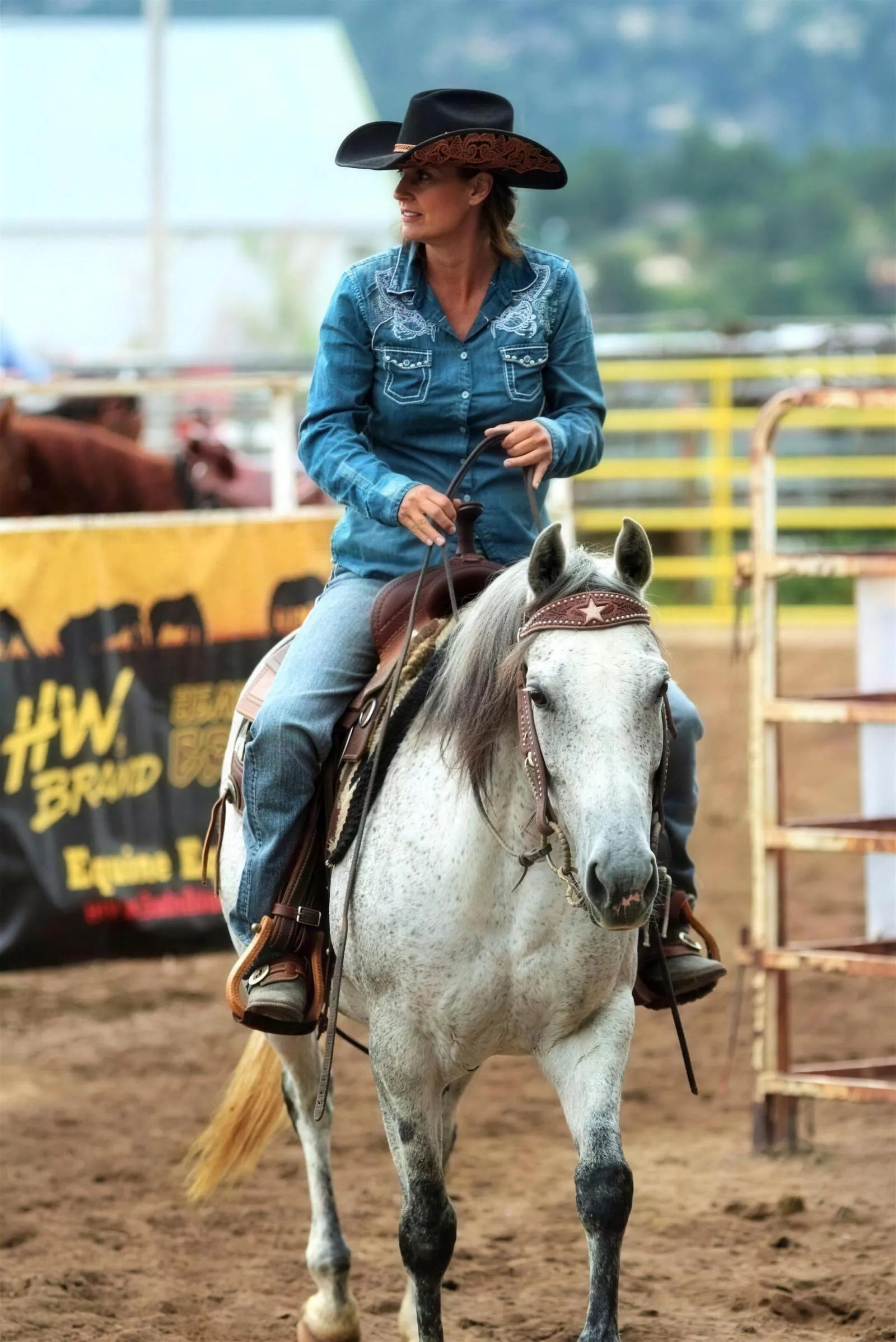 Stephanie riding her grey horse at a rodeo, in a cowboy hat and denim shirt.