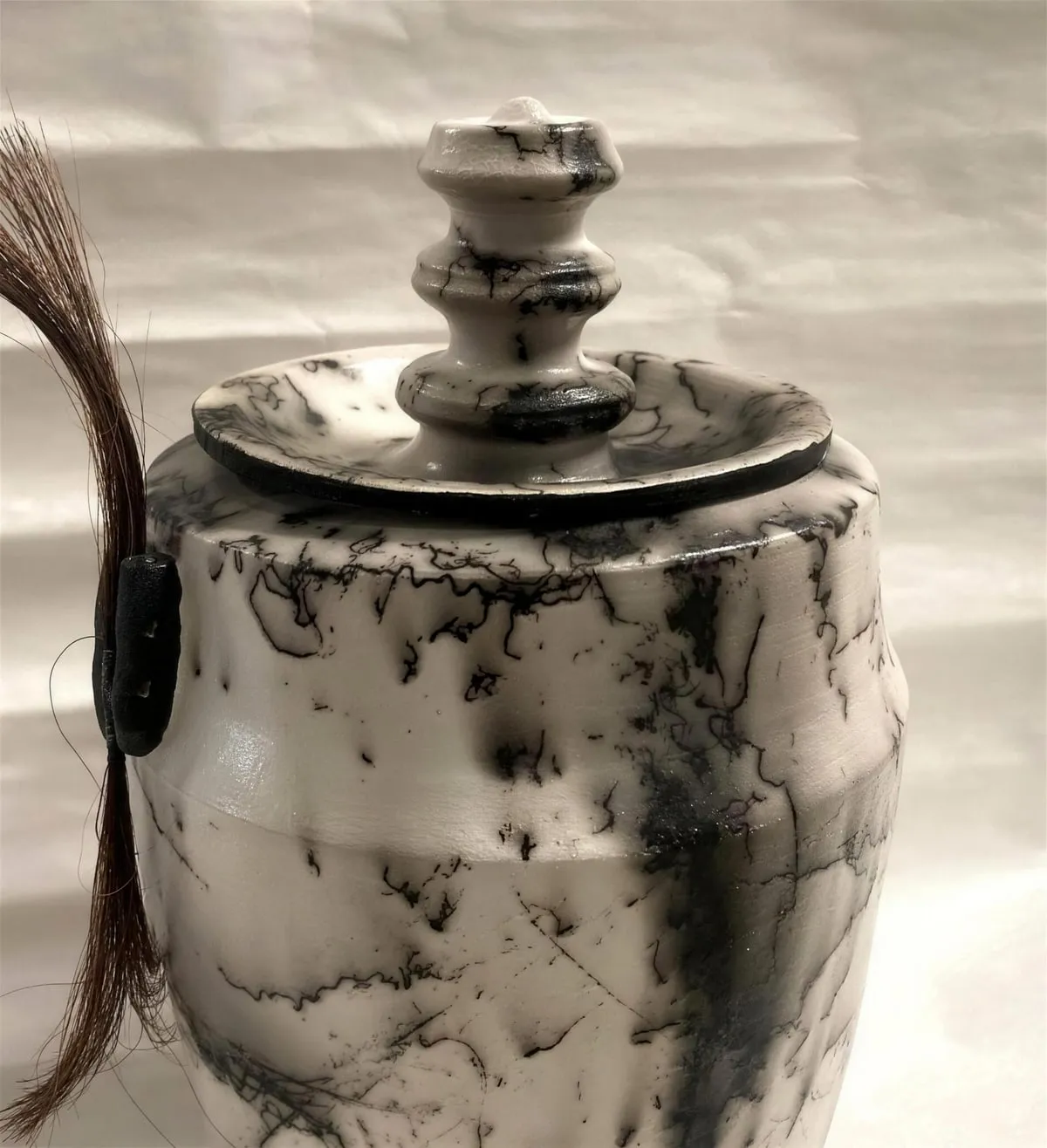 A horsehair raku urn, its white glaze marked with black traces left by the animal's own hair.